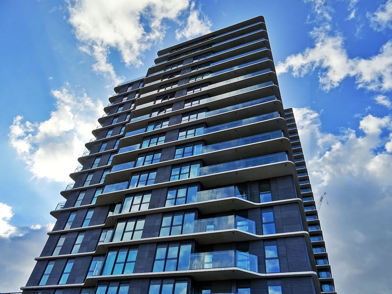 A contemporary skyscraper with glass windows and balconies under a partly cloudy sky.